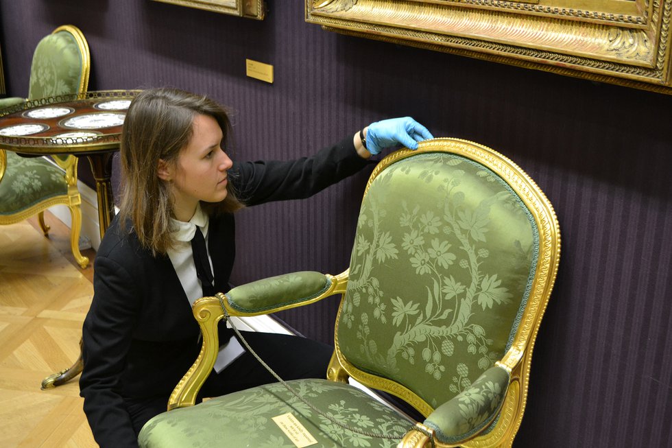 A curator checking a green decorative chair in the museum
